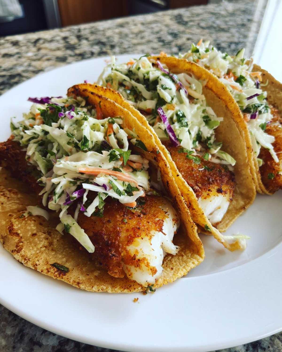 Close-up of three Crispy Baked Fish Tacos loaded with flaky fish and vibrant lime slaw on a white plate.