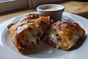 One of the Crispy Baked Reuben Egg Rolls is cut open showing melted Swiss cheese and corned beef filling.