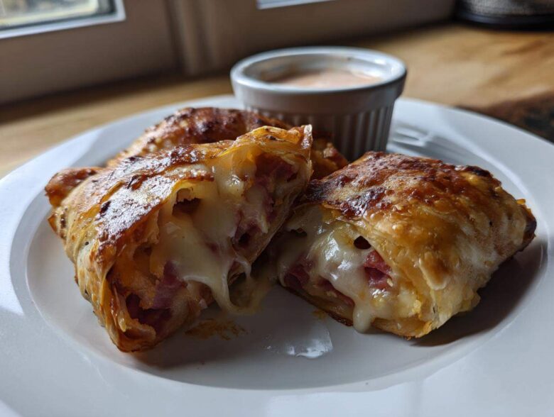 One of the Crispy Baked Reuben Egg Rolls is cut open showing melted Swiss cheese and corned beef filling.