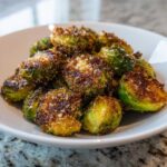 A close-up of perfectly roasted Crispy Parmesan Brussels Sprouts piled high in a white bowl.