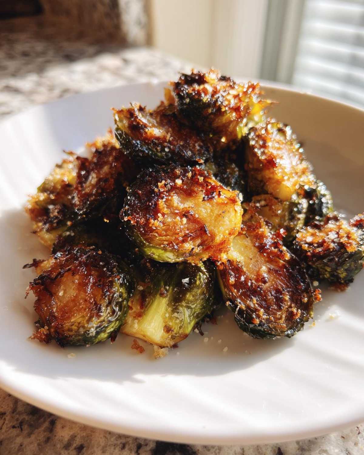 Close-up of perfectly roasted and crispy Parmesan Brussels sprouts piled on a white plate, showing caramelized edges.