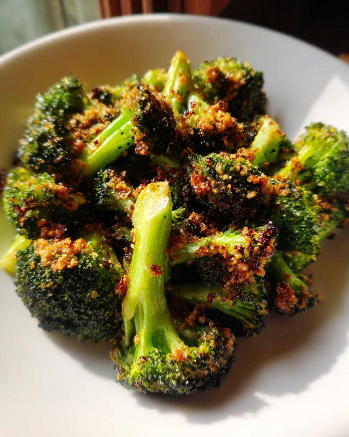 Close-up of bright green broccoli florets coated in crispy brown Parmesan topping, served in a white bowl.