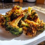 Close-up of perfectly cooked Crispy Parmesan Roasted Broccoli florets piled on a white square plate.