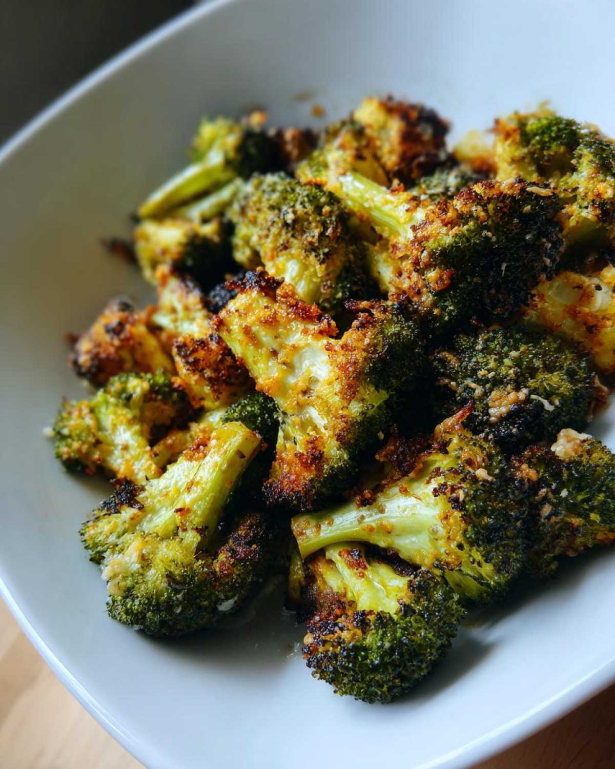 A close-up shot of perfectly roasted Crispy Parmesan Roasted Broccoli florets piled in a white bowl.