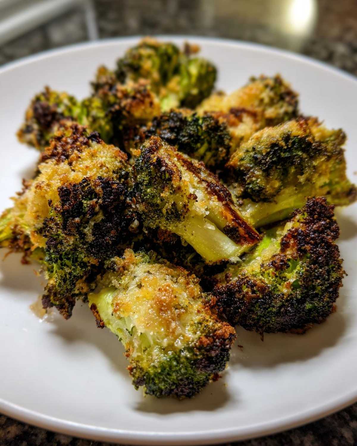 Close-up of perfectly cooked Crispy Parmesan Roasted Broccoli florets piled on a white plate.