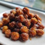 A close-up of golden brown Crunchy Air Fryer Ranch Chickpeas sprinkled with coarse salt on a small white plate.