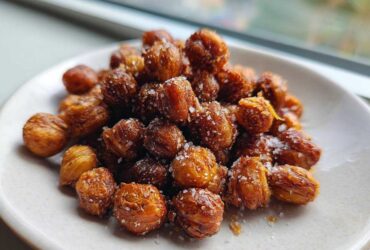 A close-up of golden brown Crunchy Air Fryer Ranch Chickpeas sprinkled with coarse salt on a small white plate.