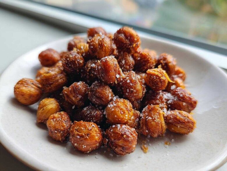 A close-up of golden brown Crunchy Air Fryer Ranch Chickpeas sprinkled with coarse salt on a small white plate.