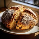 A freshly baked round of Easy Irish Soda Bread with Buttermilk and Raisins, dusted with flour and sliced.