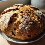 A freshly baked, round loaf of Easy Irish Soda Bread with Buttermilk and Raisins sitting on a white plate.