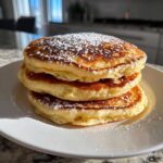 A stack of three fluffy Gluten-Free Buttermilk Pancakes dusted with powdered sugar.