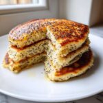 A stack of fluffy Vegan Lemon Poppy Seed Pancakes with visible poppy seeds and syrup.