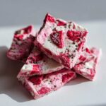 A stack of broken pieces of Frozen Strawberry Yogurt Bark featuring pink and white swirls and dried strawberries.