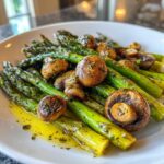 A close-up of Garlic Butter Roasted Asparagus and Mushrooms glistening in butter sauce on a white plate.