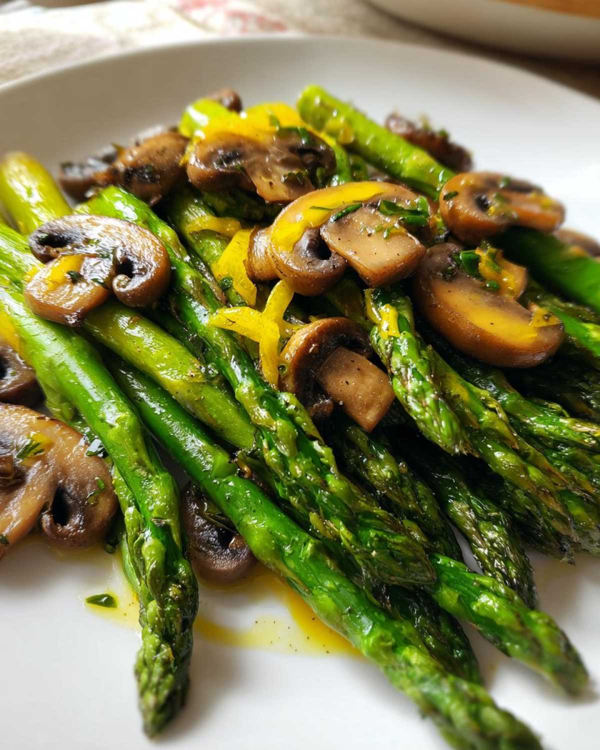 Close-up of vibrant green Garlic Butter Roasted Asparagus and Mushrooms served on a white plate.
