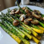 Close-up of vibrant green and yellow Garlic Butter Roasted Asparagus and Mushrooms served on a white plate.