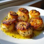 Six perfectly seared Garlic Butter Scallops with Lemon sitting in glistening garlic butter sauce on a white plate.