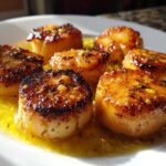 Close-up of perfectly seared Garlic Butter Scallops with Lemon resting in melted butter sauce on a white plate.