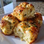 Close-up of fluffy Garlic Parmesan Pull-Apart Bread pieces stacked on a white plate, glistening with butter and herbs.