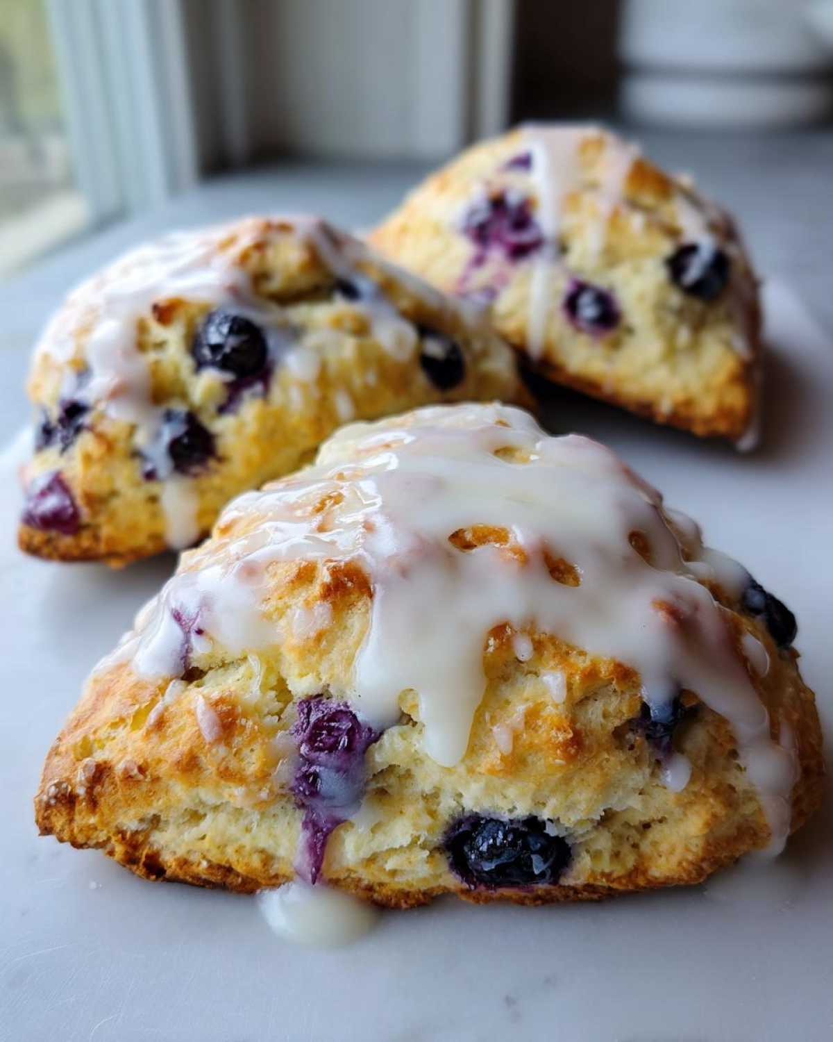 Close-up of three freshly baked Blueberry Lemon Scones topped with thick white lemon glaze.