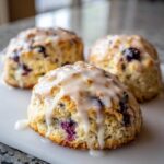 Three freshly baked Blueberry Lemon Scones topped with a thick, dripping lemon glaze.