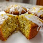 Close-up of Glazed Lemon Poppy Seed Muffins, one cut in half revealing the moist, poppy seed-flecked interior.