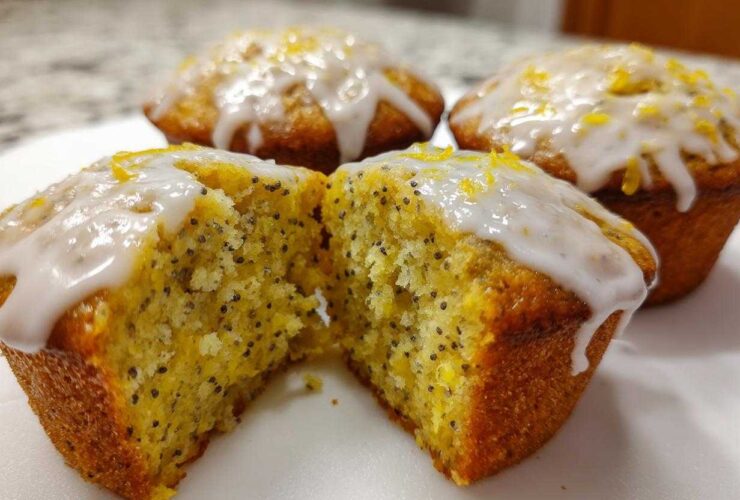 Close-up of Glazed Lemon Poppy Seed Muffins, one cut in half revealing the moist, poppy seed-flecked interior.