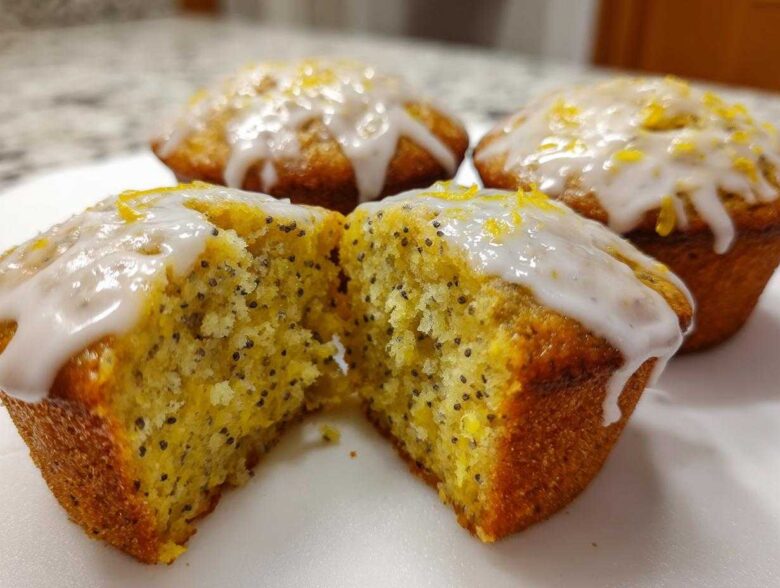 Close-up of Glazed Lemon Poppy Seed Muffins, one cut in half revealing the moist, poppy seed-flecked interior.