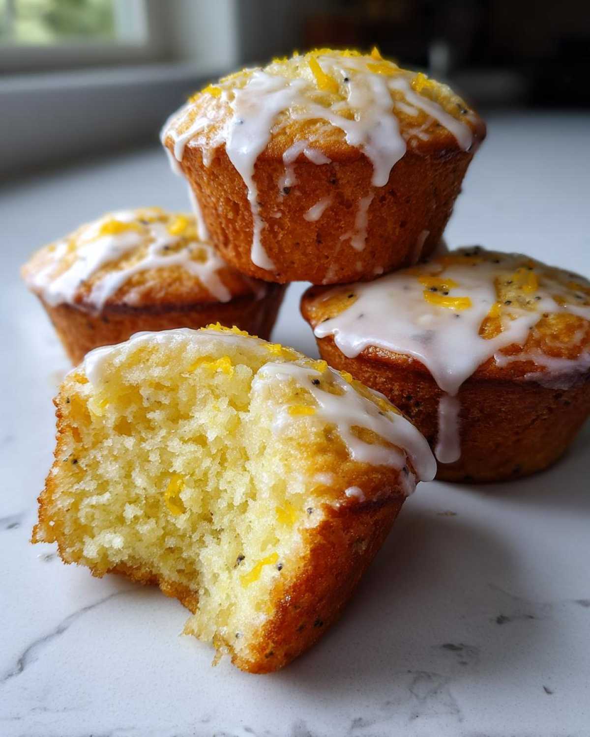 A stack of Glazed Lemon Poppy Seed Muffins, with one muffin broken open showing the moist, yellow crumb.