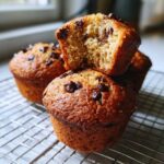 Close-up of moist Gluten-Free Banana Chocolate Chip Muffins cooling on a wire rack, one muffin broken open.