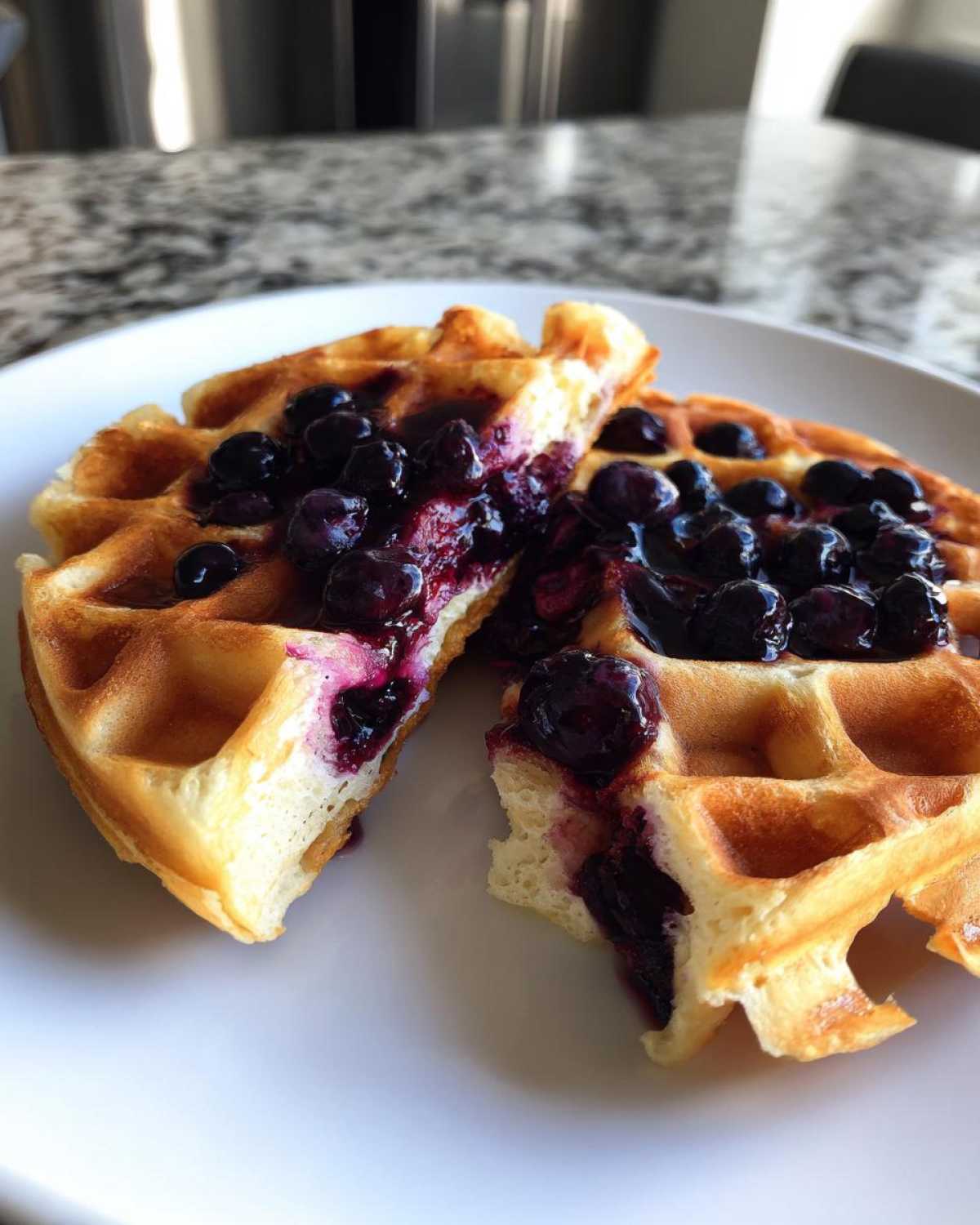 A close-up of fluffy Gluten-Free Blueberry Waffles cut in half and topped with a rich blueberry compote.