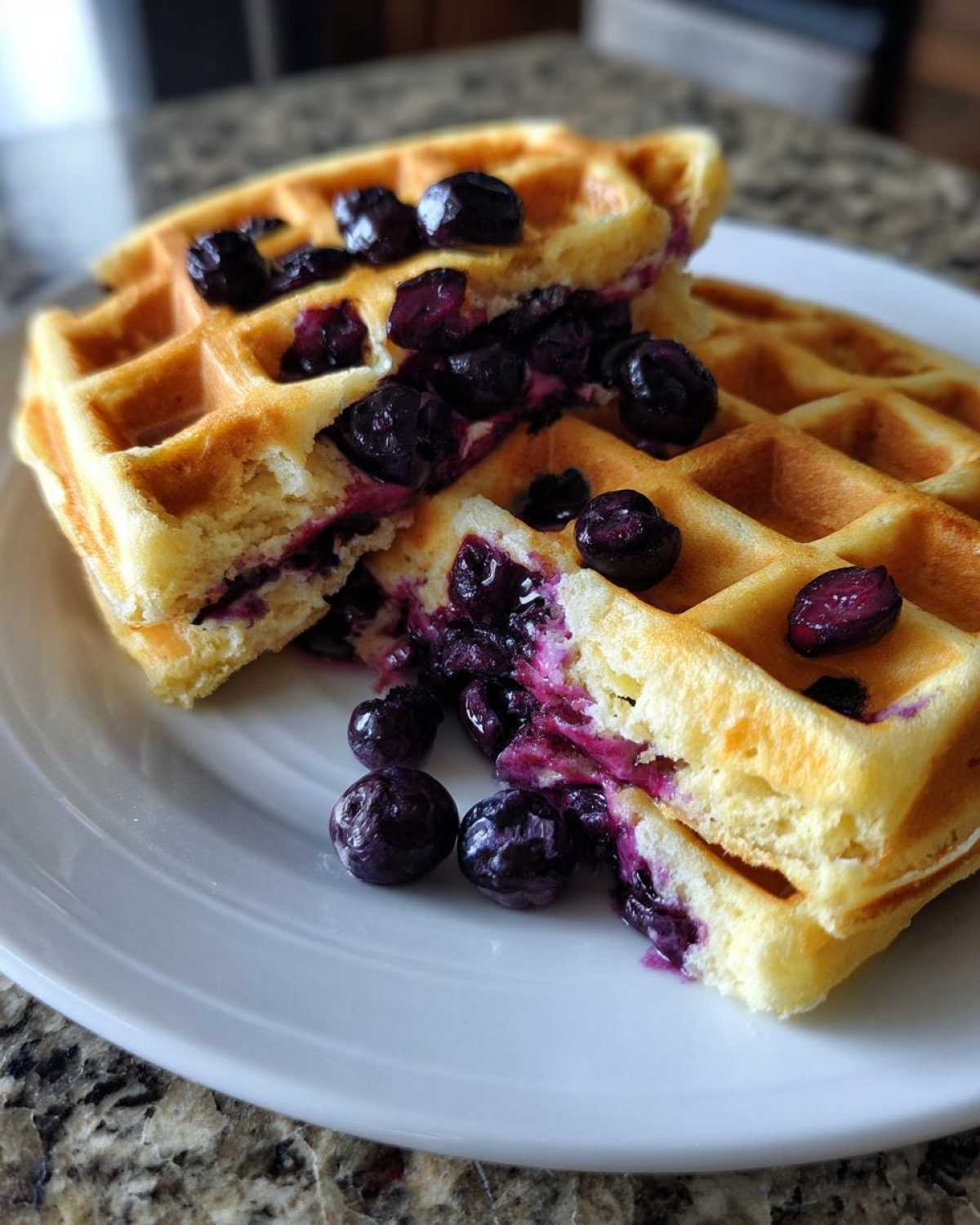Two halves of fluffy Gluten-Free Blueberry Waffles stacked and broken open, revealing cooked blueberries inside.