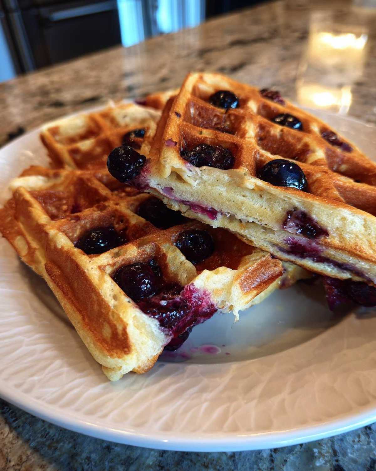 Close-up of golden Gluten-Free Blueberry Waffles, showing burst blueberries and soft interior on a white plate.