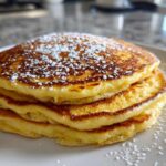 A stack of three fluffy Gluten-Free Buttermilk Pancakes dusted generously with powdered sugar on a white plate.