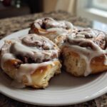 Close-up of three soft Gluten-Free Cinnamon Rolls generously topped with white icing on a white plate.