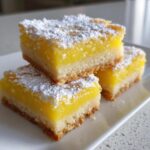 Three stacked squares of bright yellow Gluten-Free Lemon Bars with Shortbread Crust, dusted heavily with powdered sugar.