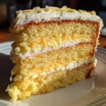 Close-up of a moist slice of Gluten-Free Lemon Coconut Cake showing three layers and white frosting.