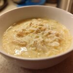 Close-up of a white bowl filled with creamy Greek Lemon Chicken Soup, featuring shredded chicken and rice.
