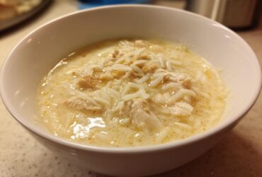 Close-up of a white bowl filled with creamy Greek Lemon Chicken Soup, featuring shredded chicken and rice.
