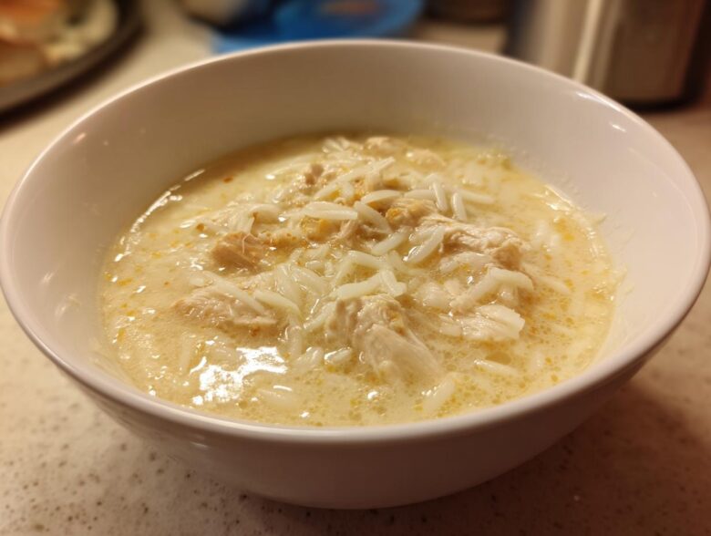 Close-up of a white bowl filled with creamy Greek Lemon Chicken Soup, featuring shredded chicken and rice.