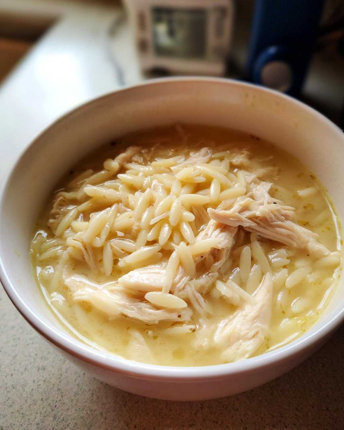 Close-up of a white bowl filled with creamy Greek Lemon Chicken Soup featuring shredded chicken and orzo pasta.