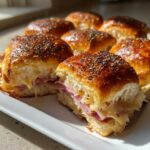 Close-up of freshly baked Hawaiian Roll Ham and Cheese Sliders with melted cheese oozing out and poppy seed topping.