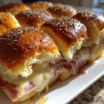 Close-up of gooey Hawaiian Roll Ham and Cheese Sliders with melted Swiss cheese and poppy seeds on top.