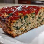 A thick slice of Healthy Turkey Spinach Meatloaf topped with a glossy ketchup glaze, showing visible spinach pieces.