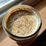 Overhead close-up of High-Protein Peanut Butter Overnight Oats in a glass jar, topped with spices.