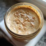 Overhead view of High-Protein Peanut Butter Overnight Oats topped with seeds in a glass jar.