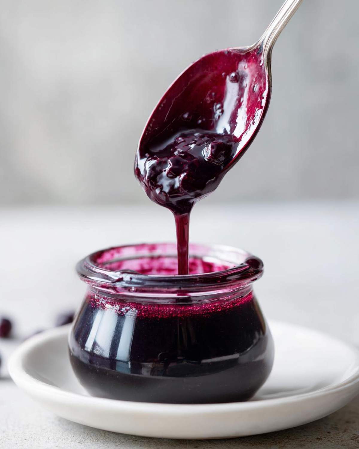 A spoonful of thick, rich Homemade Blueberry Syrup is being poured back into a small glass jar.