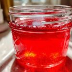 Close-up of bright red Homemade Strawberry Lemonade Concentrate stored in a glass mason jar.