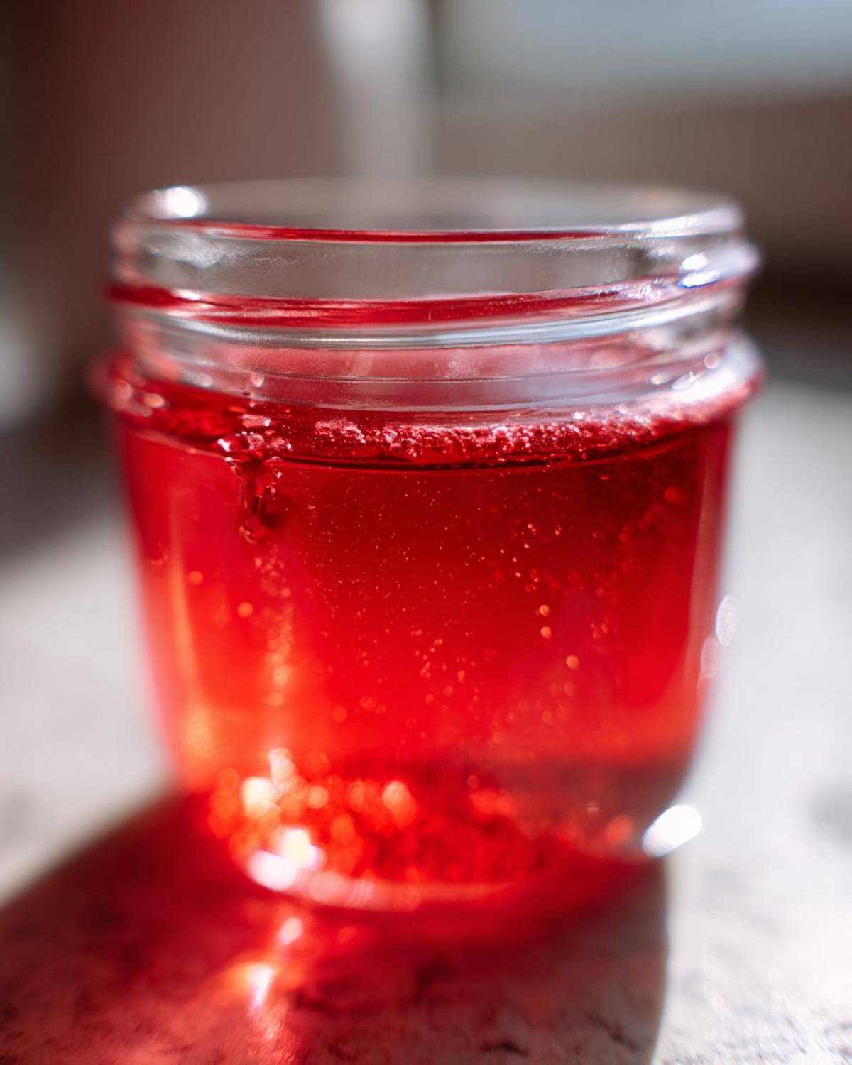 Close-up of bright red Homemade Strawberry Lemonade Concentrate stored in a small glass jar.
