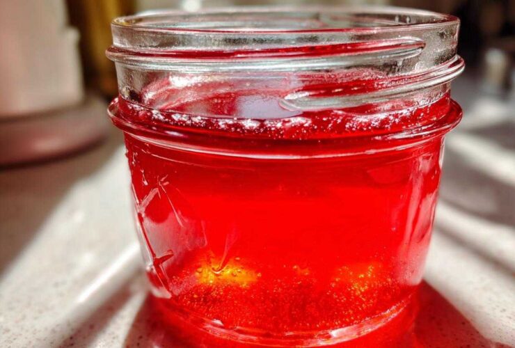 Close-up of bright red Homemade Strawberry Lemonade Concentrate stored in a glass mason jar.